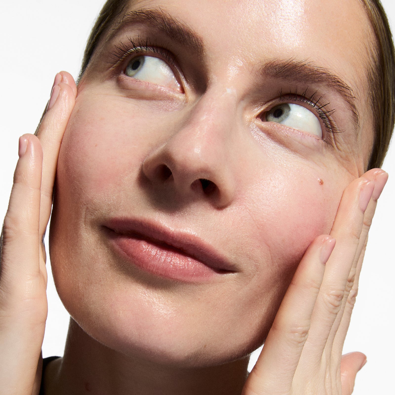 Close-up of a woman's face with hands gently touching her cheeks against a white background