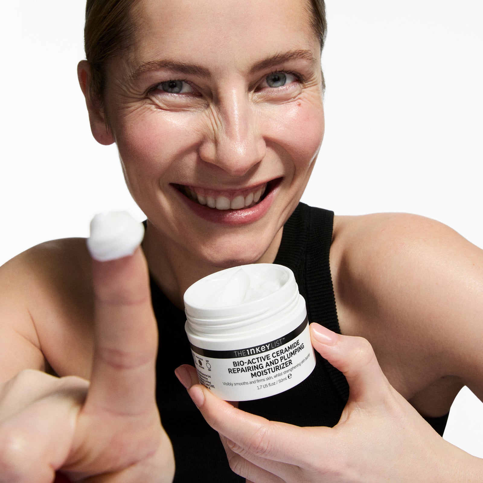 Woman holding BioActive Moisturizer and showing a white substance on her finger against a white background