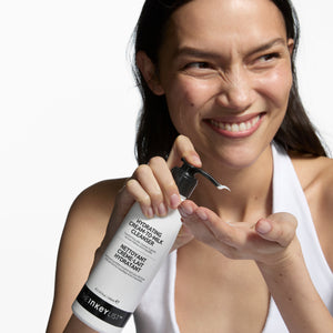 Woman holding a bottle of Inkey List hydrating cream-milk cleanser with a white background