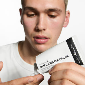 Person holding a container of The Inkey List Omega Water Cream against a white background