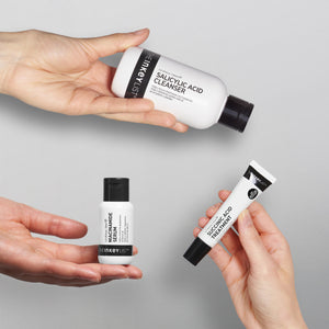An image of hands holding each product from the Clearer Skin Trio against a grey background