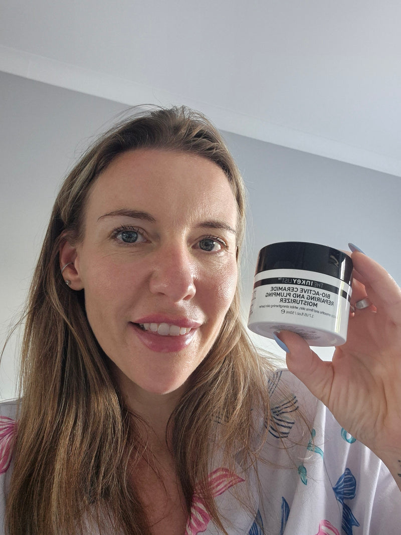 A woman holding up a jar of Bio Active Cream against a plain indoor wall background.