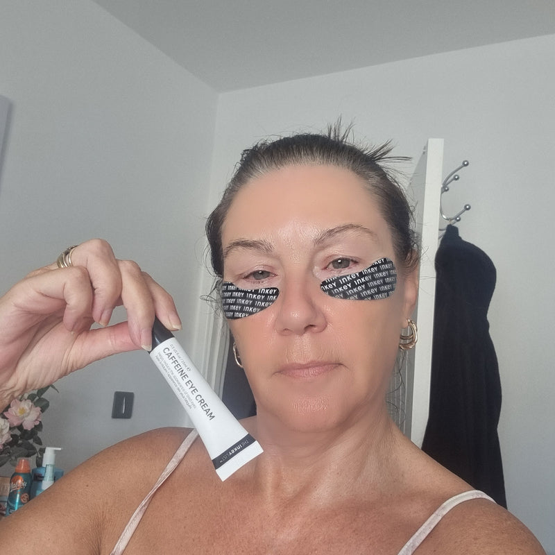 A woman holding a white tube of caffeine eye cream in front of her face.