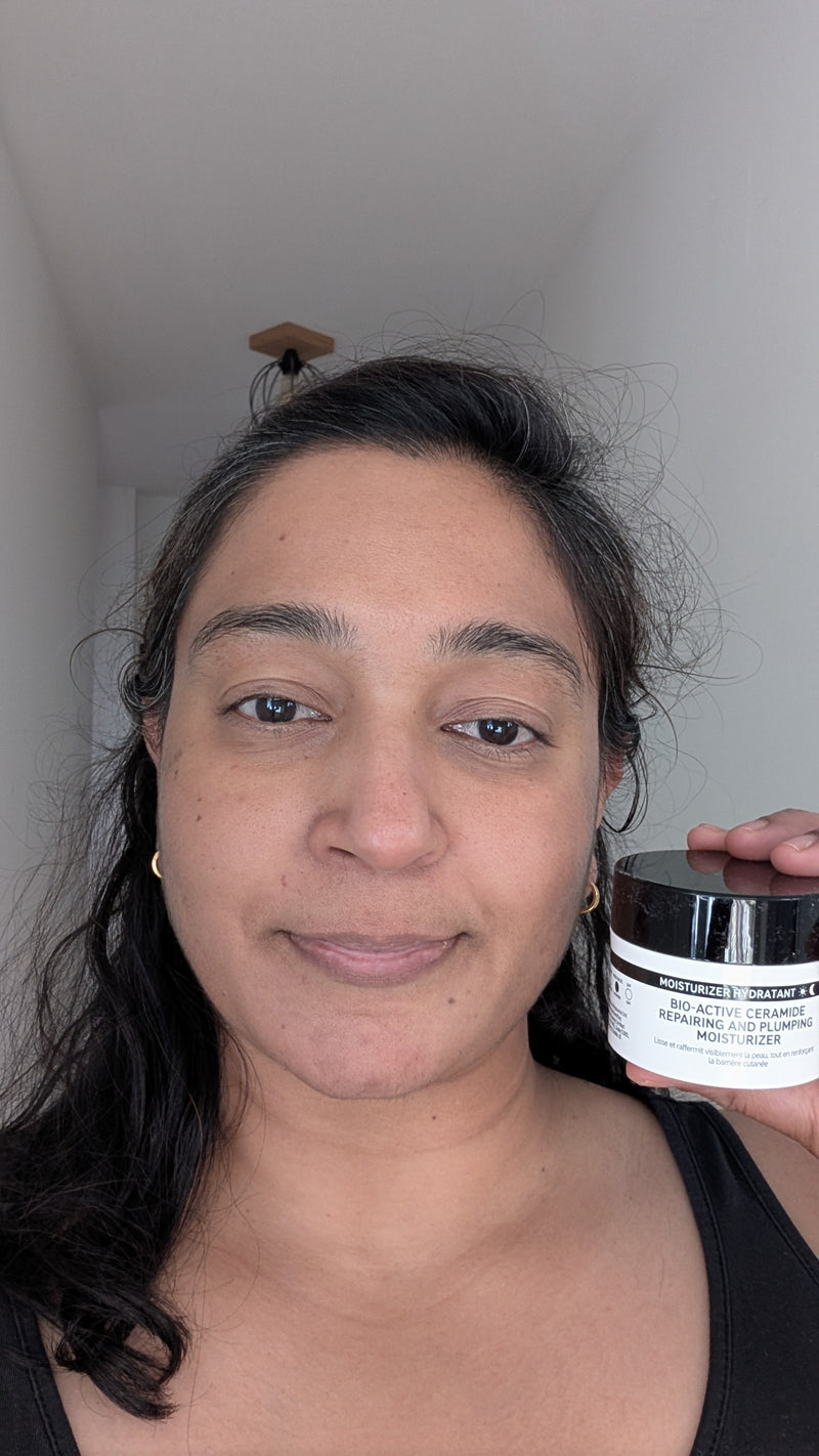 A woman holding a jar of 'Bio Active Ceramide moisturiser' in a home setting with a white wall and ceiling visible.
