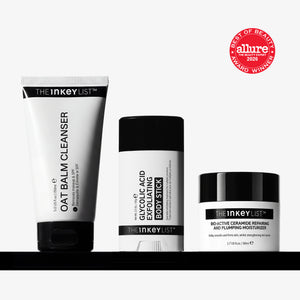 Three skincare products from The Inkey List are displayed on a black shelf against a light gray background: an oat balm cleanser tube, a glycolic acid body stick, and a ceramide moisturizing jar. A red Allure Best of Beauty 2025 award sticker is shown in the top right corner.