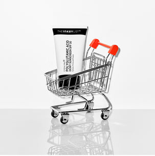 Miniature shopping cart with a tube of sunscreen on a white background