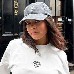 Person wearing a gray cap and white sweatshirt with 'No BS Skincare Club' branding.