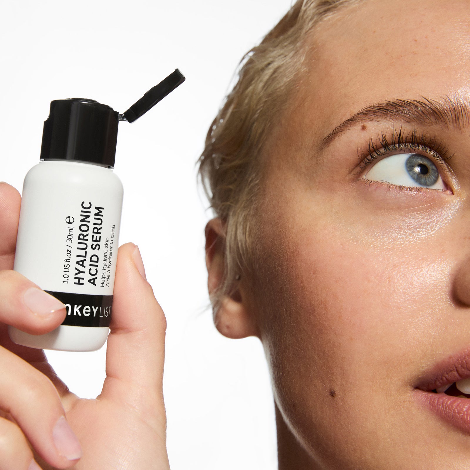 Person holding a skincare serum bottle with a close-up of their eye.