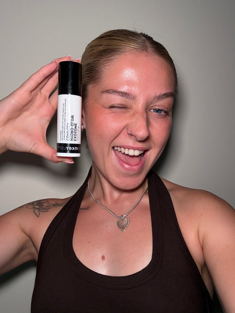 A woman holding up a white and black Exosome Serum against a plain gray wall.