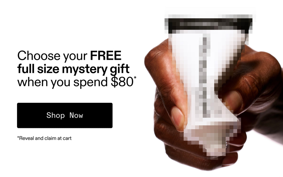 Hand holding a small container with promotional text for a free full-size mystery gift when spending $80.