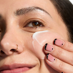 Close-up of a woman applying cream to her face with a focus on skincare.