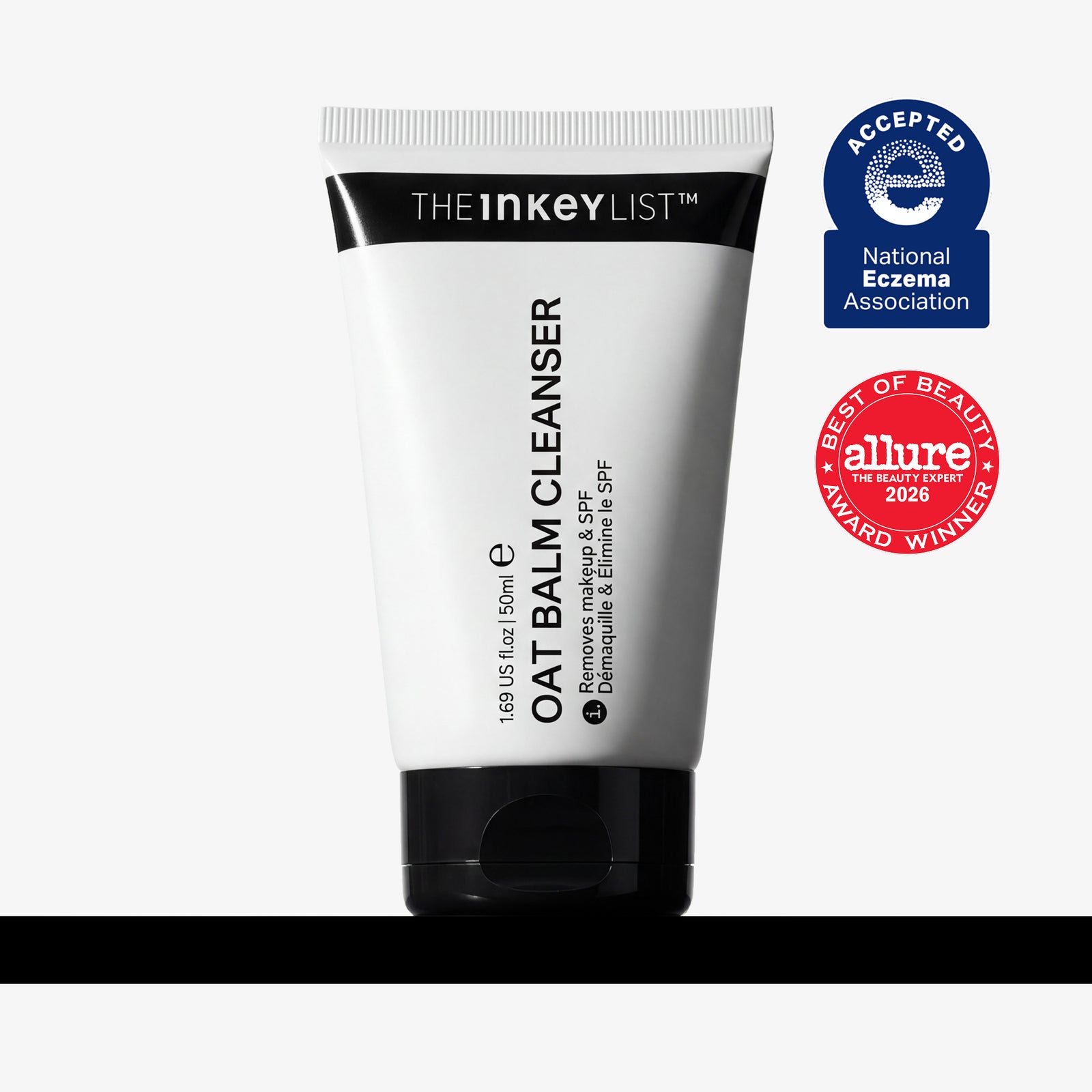 A white squeeze tube of The Inkey List Oat Balm Cleanser with a black cap, shown on a light gray background with a black bar at the bottom. Two award badges are displayed on the right: a blue National Eczema Association 'Accepted' badge and a red Allure 'Best of Beauty' award badge.