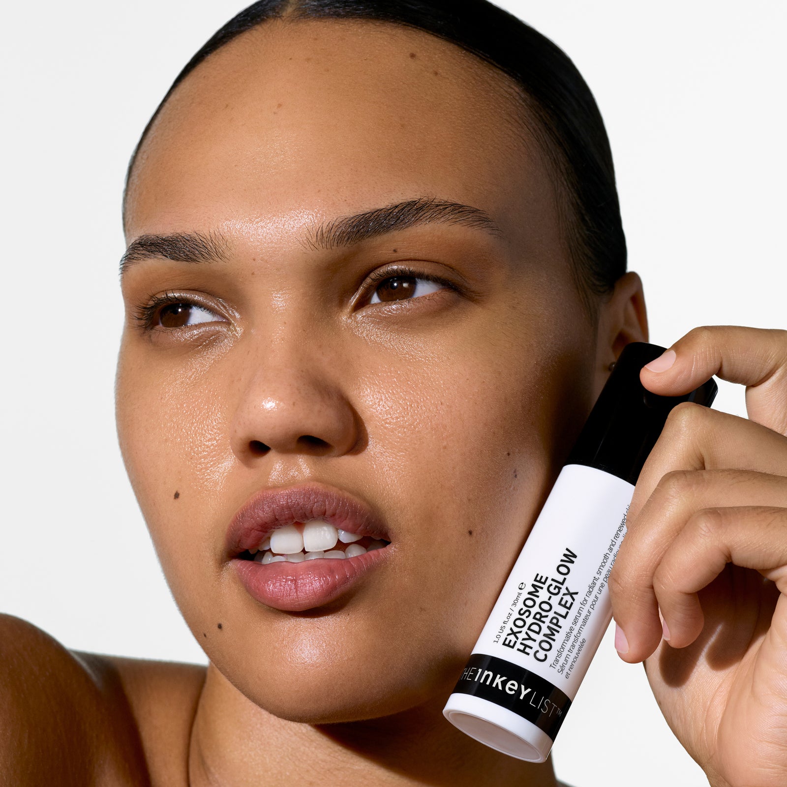 Woman holding a Exosome Hydro-Glow Complexclose to her face against a white background