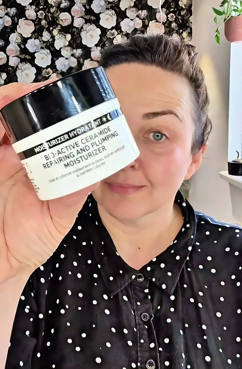 A woman holding up a jar of Bio-Active Ceramide Repairing and Plumping Moisturizer in front of her face, wearing a black and white polka dot shirt.